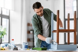 furniture renovation, diy and home improvement concept - man in gloves with paint brush painting old wooden table in grey color