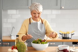 healthy eating, food cooking and culinary concept - happy smiling senior woman making vegetable salad on kitchen at home