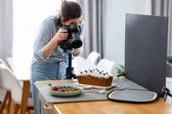 blogging, profession and people concept - female food photographer with camera photographing cake in kitchen at home