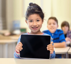 education, elementary school, technology, advertisement and children concept - little student girl showing blank black tablet pc computer screen over classroom and classmates background