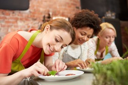 cooking class, friendship, food and people concept - happy women cooking and decorating plates with dishes in kitchen