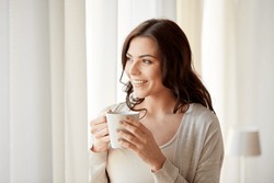 people, drinks and leisure concept - happy young woman with cup of tea or coffee at home