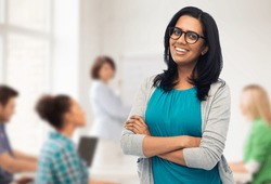 education, high school and people concept - happy smiling young indian woman or teacher in glasses over classroom background