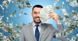 business, people and finances concept - smiling businessman with bundle of american dollar cash money over blue background