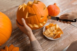 halloween, decoration and holidays concept - close up of woman with knife carving pumpkin or jack-o-lantern at home