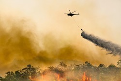 Silhouette firefithing helicopter dumps water on forest fire