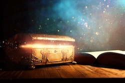 image of open antique book and gold treasure chest on wooden table with glitter overlay