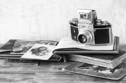 vintage camera, antique photographs and books over wooden table. black and white photo.