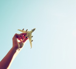 close up photo of woman's hand holding toy airplane against blue sky . image is retro filtered 
