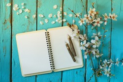 top view image of spring white cherry blossoms tree, open blank notebook  next to wooden colorful pencils on blue wooden table. vintage filtered and toned image