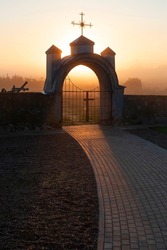 Church architecture. A stone gate with an arch and a Catholic cross above it. Morning. fog 