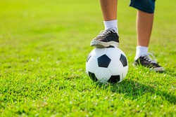Closeup legs of child holding the soccer ball on the football field