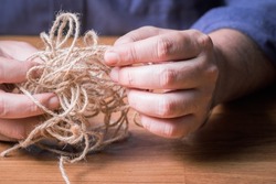 Closeup man try to fix the problem of tangled jute rope, make it easy concept, or psychotherapy