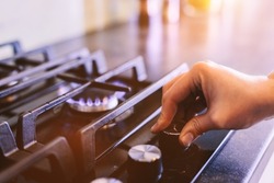 Hand turning on gas burner on kitchen stove top.