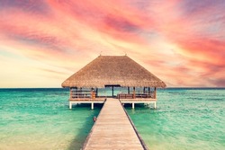 Beach in Maldives at sunset, wooden jetty and small shed. Exotic holiday destination