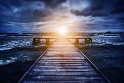 Old wooden jetty during storm on the ocean. Abstract light at the end. Concept of hope, future, religion, god etc.
