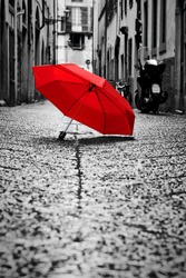 Red umbrella on cobblestone street in the old town. Wind, rain, stormy weather. Color in black and white conceptual, idea. Vintage, retro style.