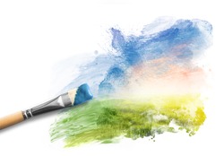 Painting the spring landscape. Brush with blue paint over sky and green field. Concept of creating art, creativity, imagination.