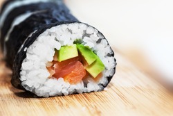 Sushi with salmon, avocado, rice in seaweed and chopsticks on wooden table. Japanese, Asian healthy food.