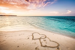 Two hearts drawn on a sandy beach by the sea. Sunset view. Love symbol.