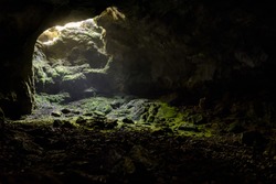 Dark cave with a bright daylight spot of exit. Natural cave opening in Crimea. Entrance to the karst cave in a mountain. Inside the subterranean cave background with copy space. 
