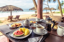 Breakfast on sea beach, table setting with vegan food in hotel restaurant. Buffet with fruits and coffee in cafe outdoor in tropical resort. Concept of travel and vacation in Caribbean or Sri Lanka.