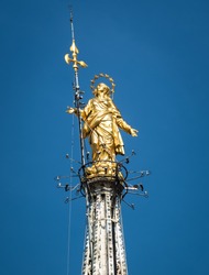 Madonna or Madonnina atop Milan Cathedral at height of 108.5 m, Milan, Italy. Vertical view of golden statue on blue sky background. Nice Gothic architecture, Duomo di Milano is top landmark of Milan