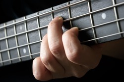 Bass guitar player hand close-up, concept of playing on bass electric guitar, live music and skill. Guitarist fingers on bass fretboard or fingerboard and frets. Lesson and practice theme.