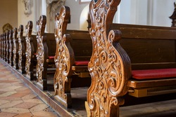 Empty pews inside church close-up, carved wooden pews in catholic cathedral, detail of Christian church interior. Beautiful old pews, worship benches in sanctuary. Prayer, faith and service concept.