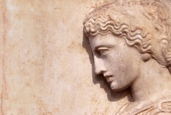 Ancient Greek relief of woman on marble wall with copy space for text. Remains of culture of past civilization in Greece. Beautiful stone sculpture, side view of face, old Greek art background.