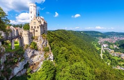 Lichtenstein Castle on mountain top in summer, Germany, Europe. This famous castle is landmark of Schwarzwald, Baden-Wurttemberg. Scenic view of fairytale Lichtenstein Castle and city in distance. 