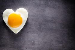 Fried egg heart-shaped and gray background.