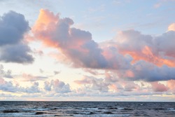 Clear sky with lots of glowing colorful pink cumulus clouds above the Baltic sea shore after thunderstorm at sunset. Dramatic cloudscape. Warm golden sunlight. Picturesque scenery. Fickle weather