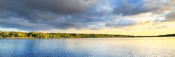 Dramatic sunset sky with glowing golden cirrus and cumulus clouds above the river and forest before the rain. Idyllic rural scene. Panoramic view. Vacations, eco tourism, nature of Scandinavia