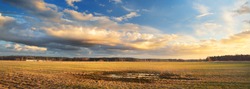 Agricultural field under the colorful sunset cumulus clouds after the rain, golden sunlight. Dramatic cloudscape. Idyllic rural landscape. Picturesque panoramic scenery