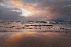Panoramic view of the Baltic sea from a sandy shore. Clear sunset sky, colorful glowing pink clouds, soft light. Symmetry reflections on water, natural mirror. Weather, winter, climate change, nature