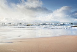 Panoramic view of Baltic sea from sandy shore (sand dunes). Dramatic sky with glowing clouds, sunbeams. Waves, water splashes. Idyllic seascape. Warm winter weather, climate change, nature. Denmark
