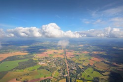 Clear blue sky with glowing cumulus clouds above the village, agricultural field, forest and sea shore on a sunny day. Panoramic aerial view from plane. Germany. Summer landscape. Nature, environment