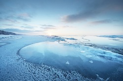 Frozen Baltic sea shore at sunset. Ice fragments close-up, snow-covered pine forest in the background. Colorful cloudscape. Symmetry reflections on the water. Nature, climate change. Panoramic view