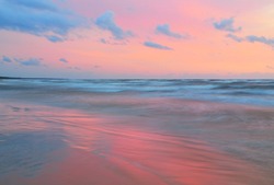 Baltic sea at sunset. Dramatic sky, blue and pink glowing clouds, soft golden sunlight. Waves, splashing water. Picturesque dreamlike seascape, cloudscape, nature. Panoramic view, long exposure
