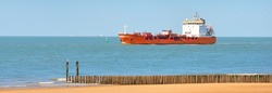 Red cargo tanker ship sailing next to the coast of Vlissingen, the Netherlands. Freight transportation, nautical vessel, fuel and power generation, logistics, industry, environment. Panoramic view