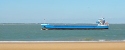 Blue cargo ship sailing to Antwerp port by the coast of Vlissingen, Netherlands. Freight transportation, nautical vessel, logistics, industry, commerce, environment. Panoramic view, copy space