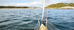 White yacht sailing in the North sea after the storm. Norway. Top down view from the deck to he bow and sails. Island (fjords) in the background. Transportation, cruise, recreation, regatta, sport