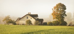 Modern brick country house (cottage) and green plowed agricultural field in a morning fog. Autumn rural scene. Architecture, agriculture, farm, ecology, countryside, ecotourism