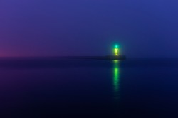 Panoramic view of Baltic sea at night. Port entrance, lighthouse, breakwaters. Thick fog, green and blue light. Waves, water splashes, long exposure. Seascape. Monochrome scenery. Danger, safety theme