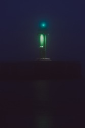 Panoramic view of Baltic sea at night. Port entrance, lighthouse, breakwaters. Thick fog, green and blue light. Waves, water splashes, long exposure. Seascape. Monochrome scenery. Danger, safety theme