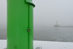 Panoramic view of Baltic sea from sandy shore. Lighthouse close-up. Thick white fog, mist, snow. Seascape. Monochrome winter scenery