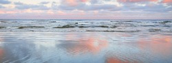 Panoramic view of the Baltic sea from a sandy shore. Clear sunset sky, colorful glowing pink clouds, soft light. Symmetry reflections on water, natural mirror. Weather, winter, climate change, nature