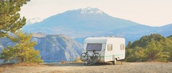 Caravan trailer parked on a mountaintop with a view on French Alps near lake Lac de Serre-Poncon. Transportation, RV, motorhome, road trip, camping, tourism, recreation, lifestyle