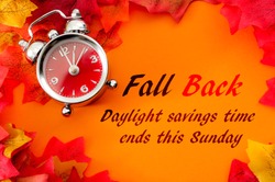 Fall back, the end of daylight savings time and turn clocks back on hour concept with a clock surrounded by dried yellow leaves with the text Fall back, daylight savings time ends this Sunday